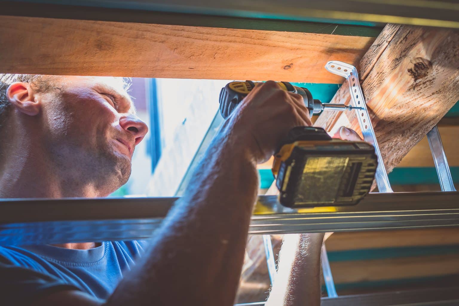 Screwing tin holders for a drywall into a wood portion of a roof using a battery powered cordless drill
